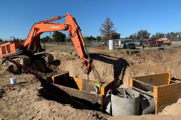 A backhoe lowers a piece of large pipe into a worksite