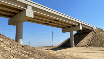 A photo of Jackson Ave Grade Separation from below, the concrete girders visible spanning over the right of way for the future high-speed rail route. Bight blue sky as background.