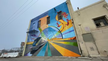 Wide shot of mural in Fresno’s Chinatown. Painting includes the conceptual rendering of CA HSR trains, an outline of California and her counties, a traditional Chinese dragon, and lines drawing the viewer toward the horizon and conceptually the future. A more detailed description of this image is available upon request to the email address info@hsr.ca.gov