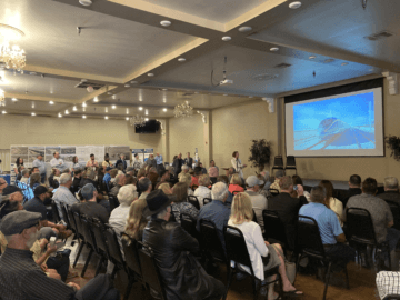 Rows of seating people looking at a screen with a rendering of a high-speed rail train as part of a presentation.