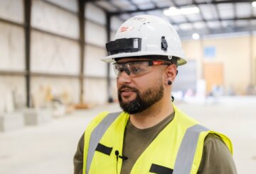 Ponyboy Gonzales stares off into the distance wearing a hard hat, safety goggles, and bright yellow vest