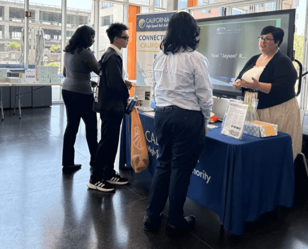 Women behind an outreach table talking to students. 