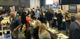An auditorium of people mingling at a Small Business event. There are booths with tables, branded tablecloths, and information.